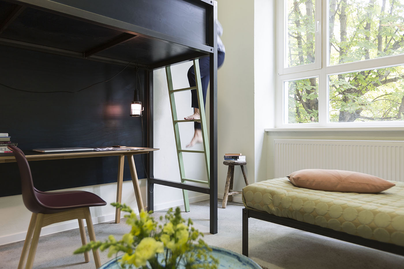 Person climbing bunk bed over desk next to large window