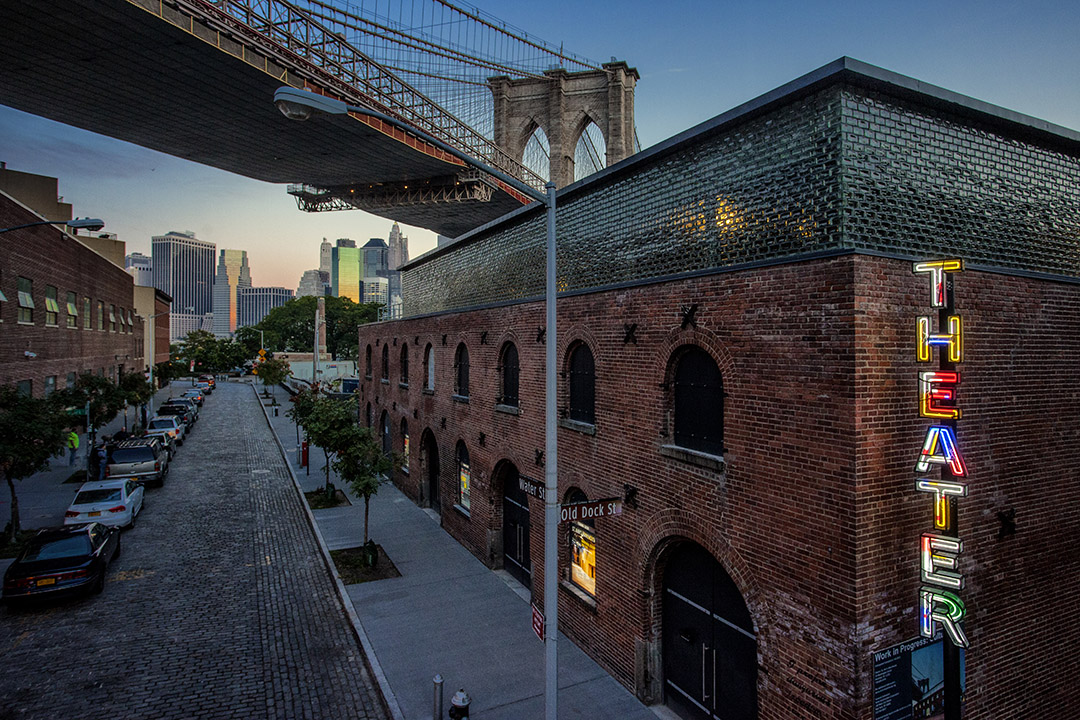 Brick building with a multicolored sign with the brooklyn bridge in the background