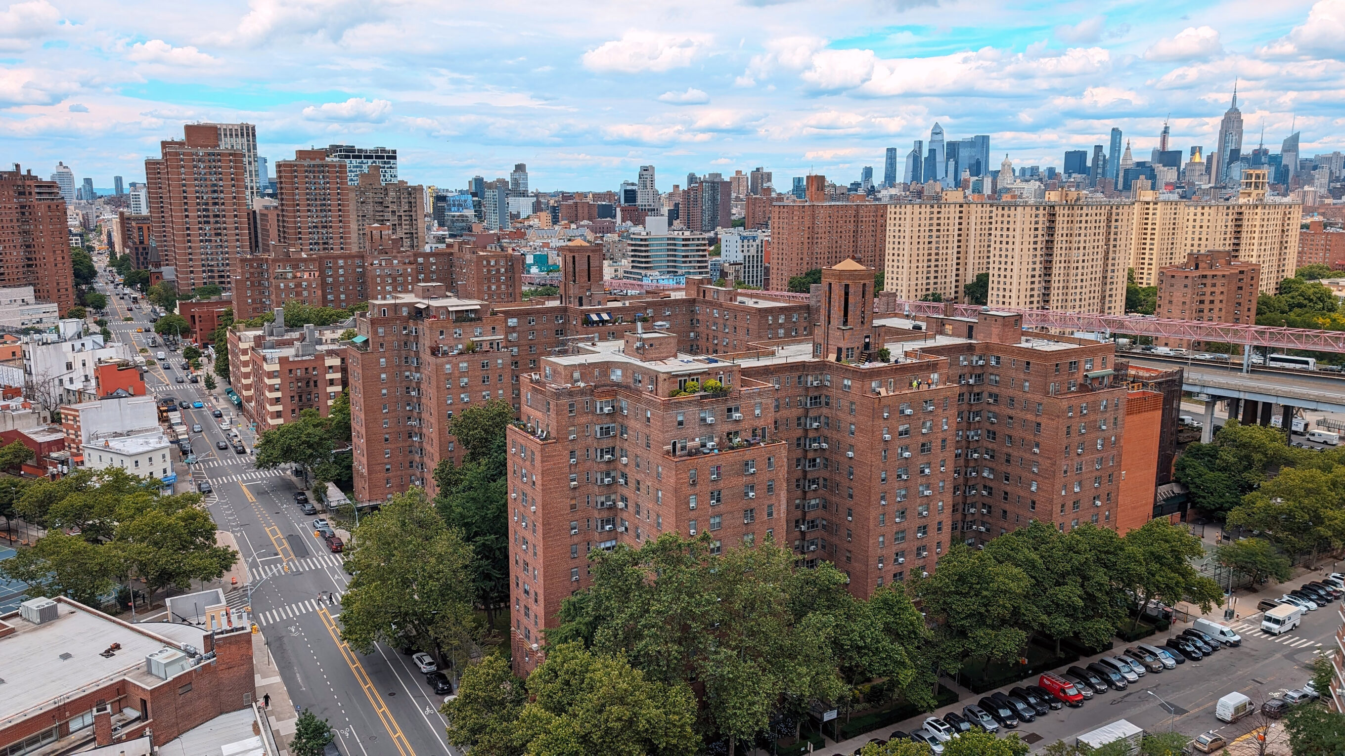 Large brick housing complex with the skyline of Midtown Manhattan in the background