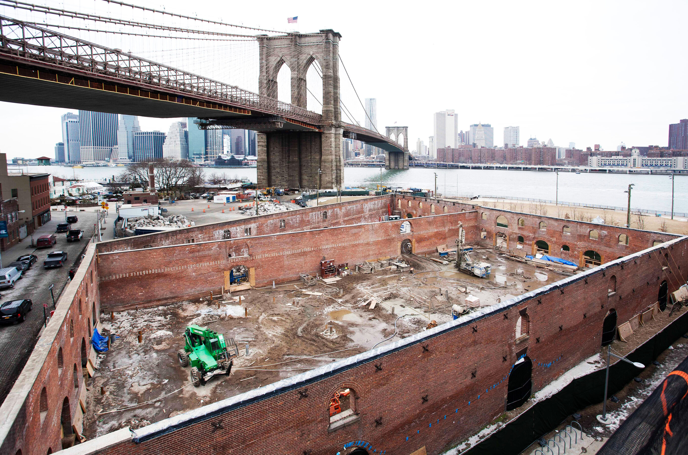 An aerial view looking over a construction site onto the east river and brooklyn bridge