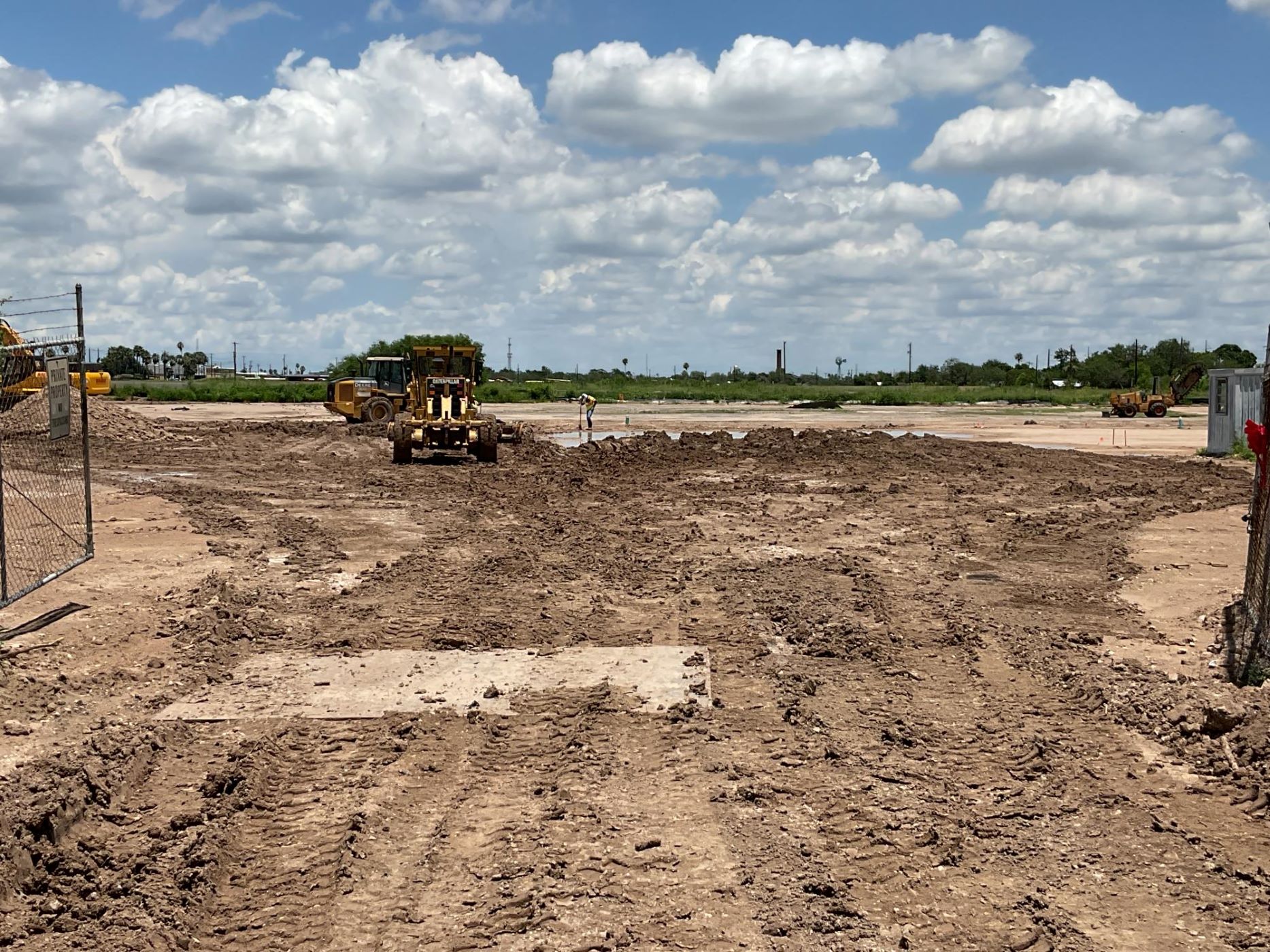 large field of dirt with construction worker and digger