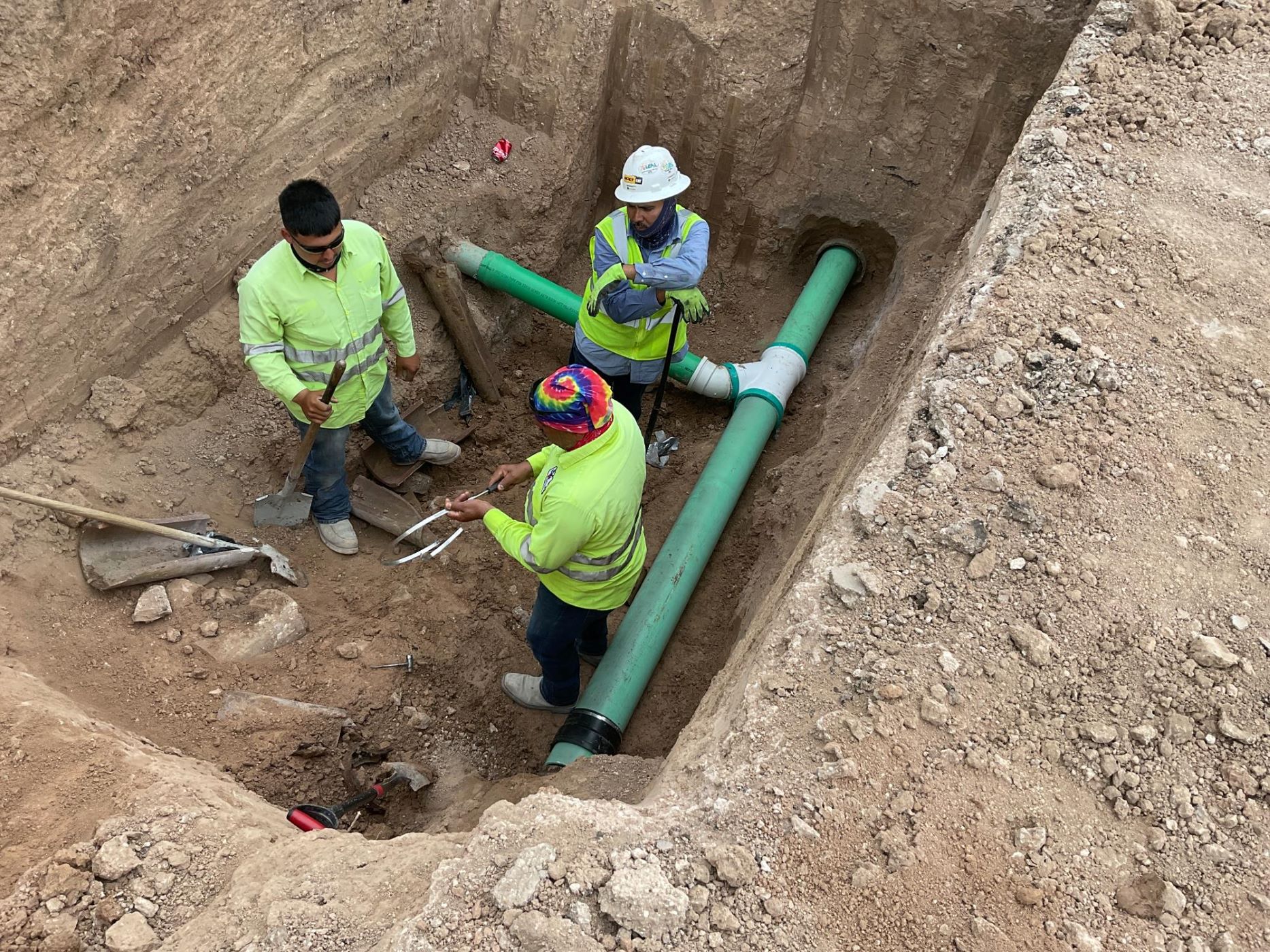 construction workers in a trench laying green pipes