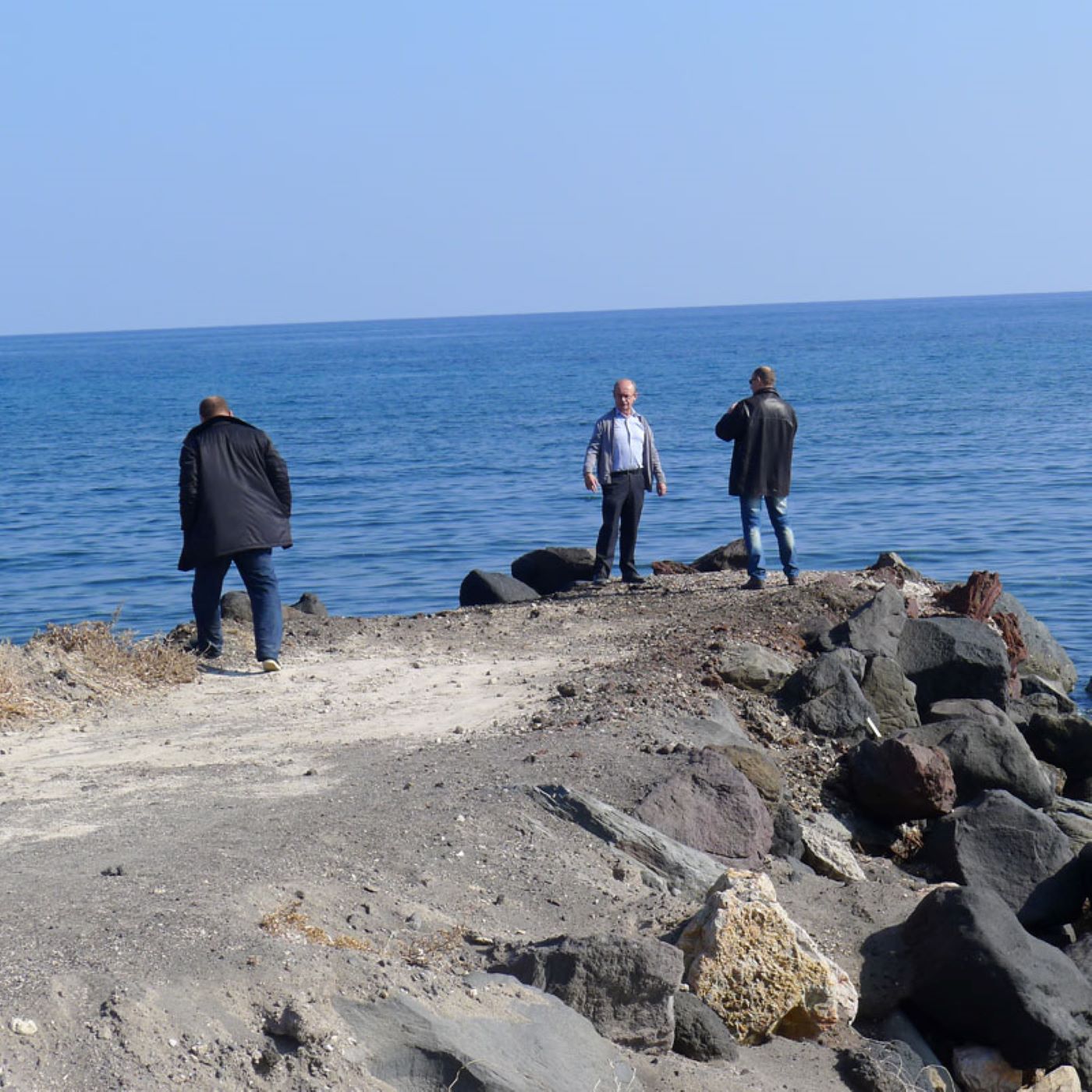 three men standing on the edge of a road overlooking the ocean