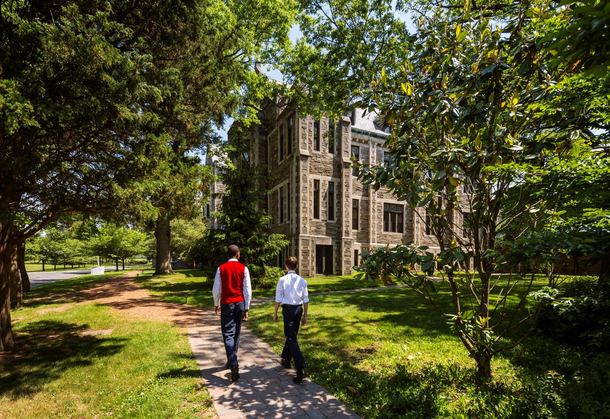 Two boys walking down a garden path towards a historic building