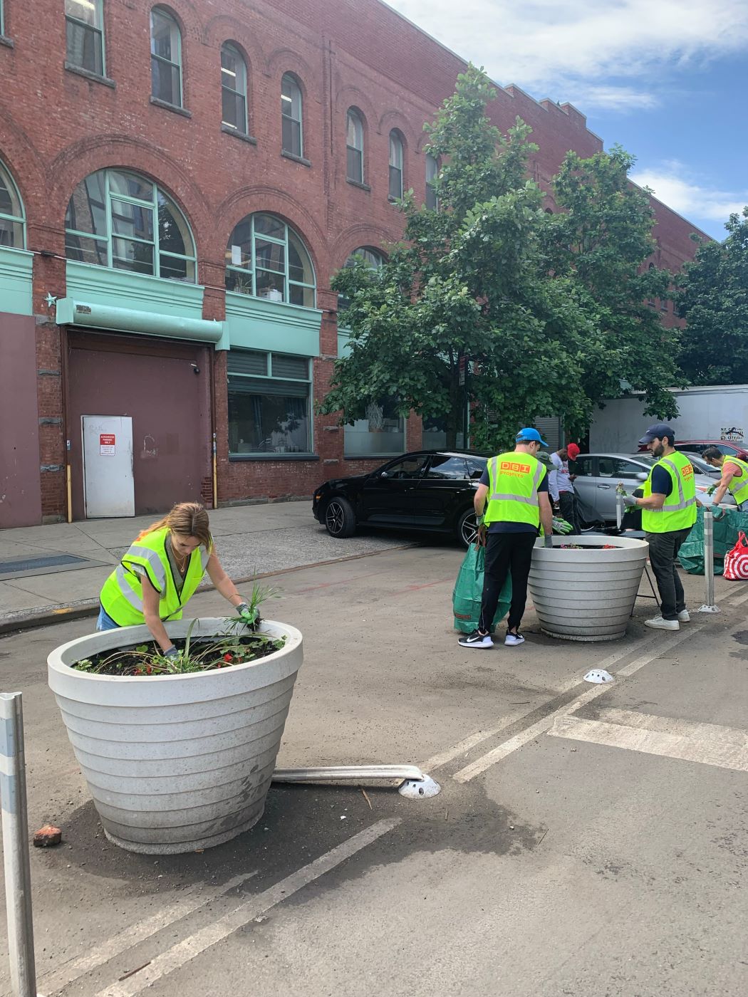 multiple people in neon yellow vests planting a tree into a large pot