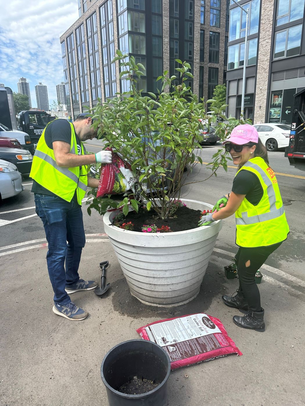 two people in neon yellow vests planting a tree into a large pot