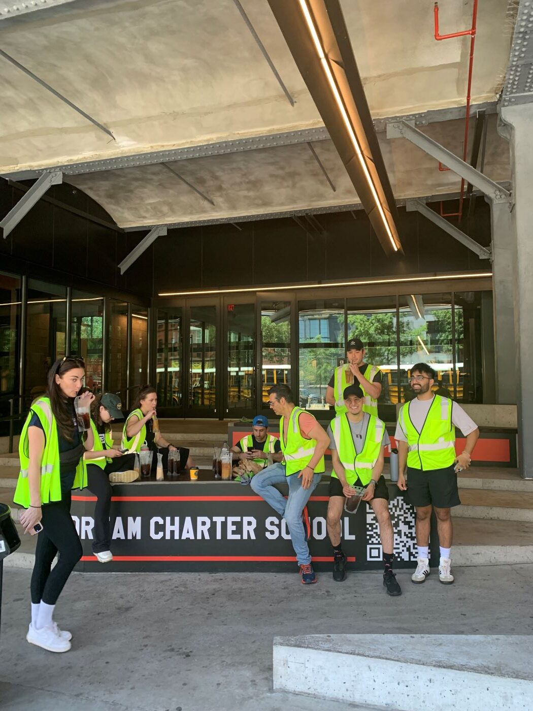 multiple people in neon yellow vests sitting on a concrete plinth drinking coffee