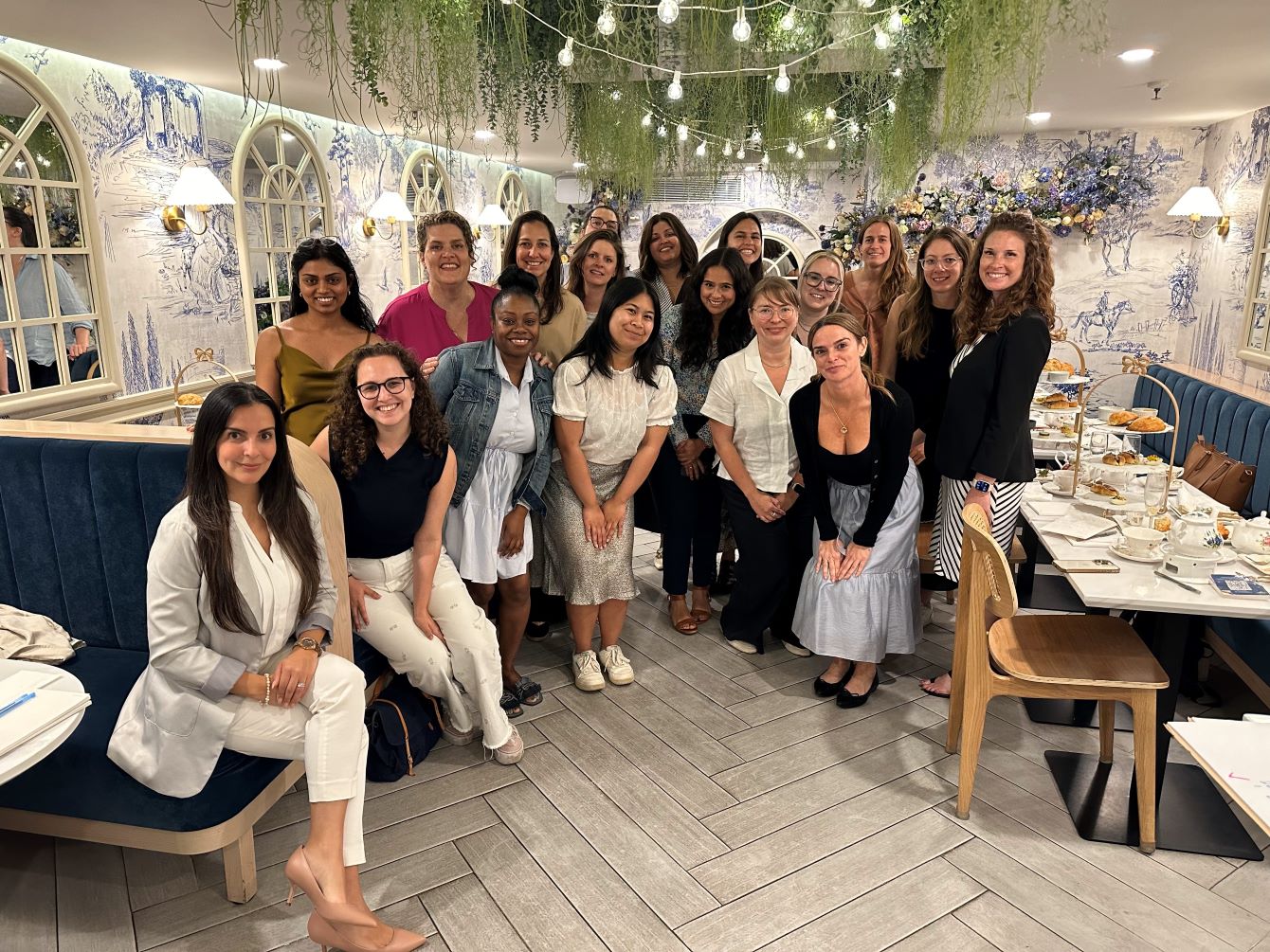 a group of women, sitting and standing, with floral wallpaper