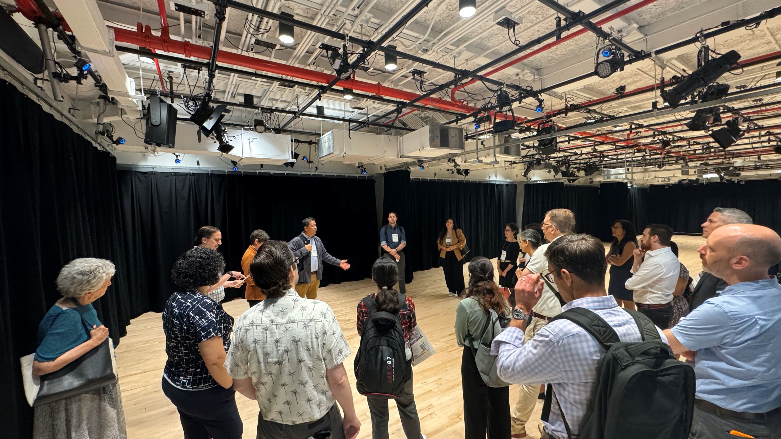 large group listening to a speaker inside, standing on timber flooring