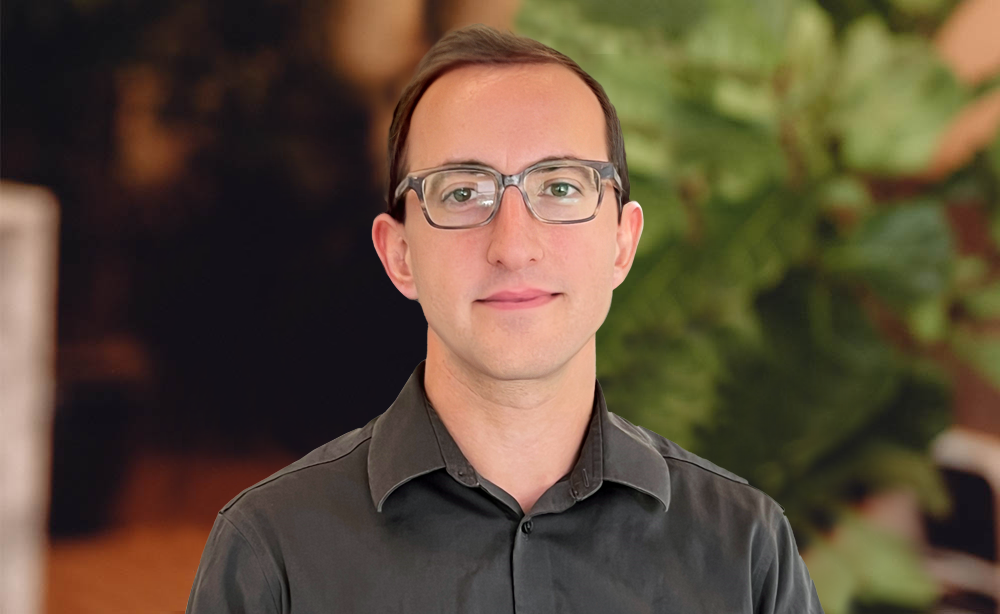 Man in glasses and collared shirt standing in front of office with plants