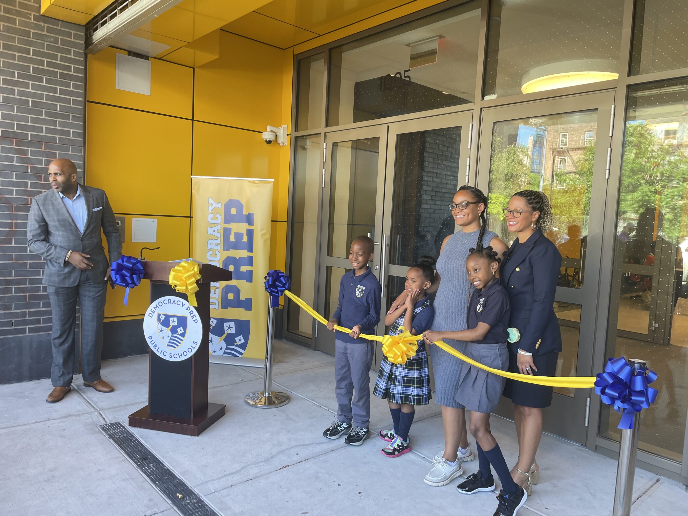 School leaders and students gather in front of the entrance to the new school to cut the ribbon