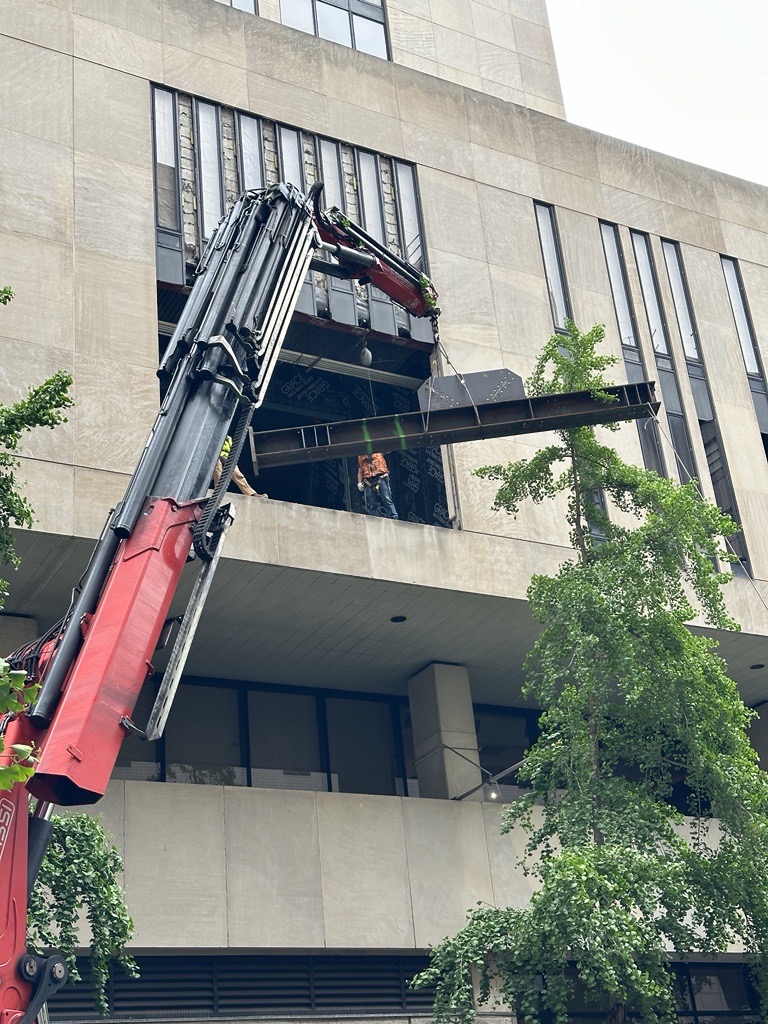 Crane lifts steel beam into window of midcentury building