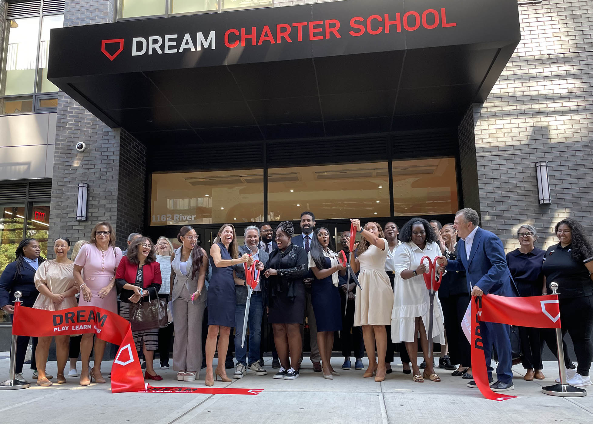 Group of people cut ribbon outside of the entrance of the new school