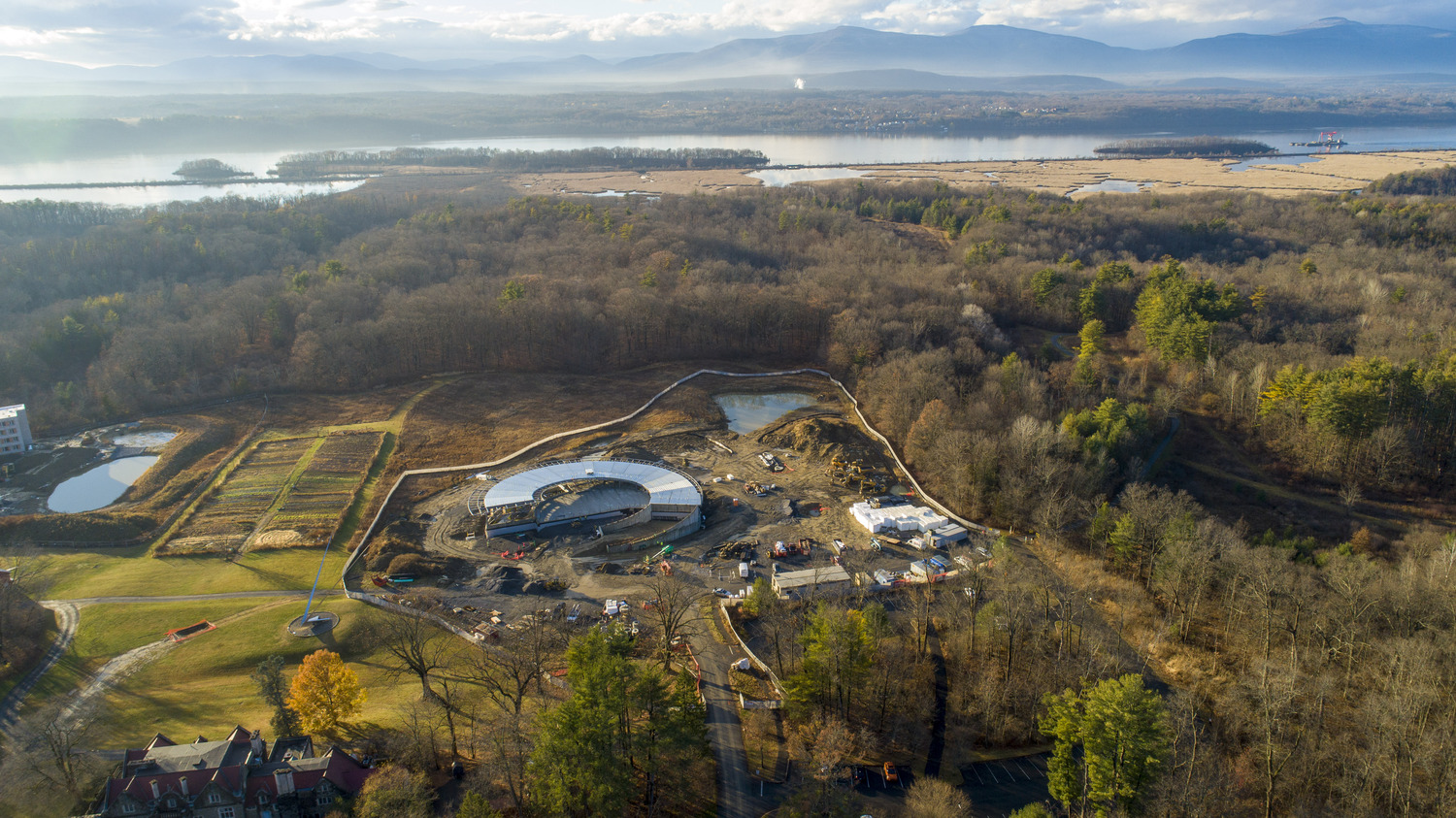 Aerial photo of circular building under construction amongst fall trees along the Hudson River