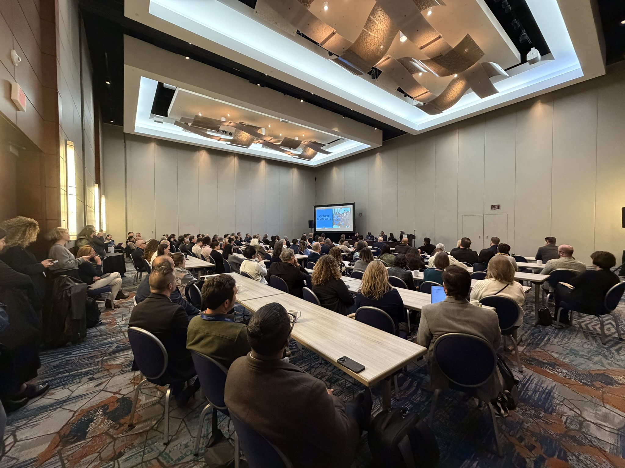 Large group of people gathered in a hotel conference room looking towards a group of presenters
