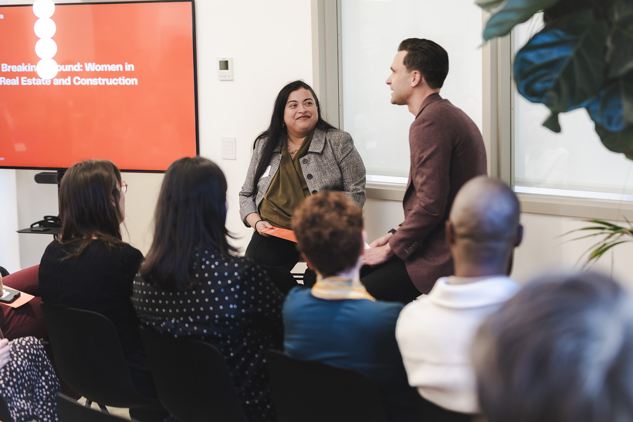 Woman and a man speaking in front of a seated crowd
