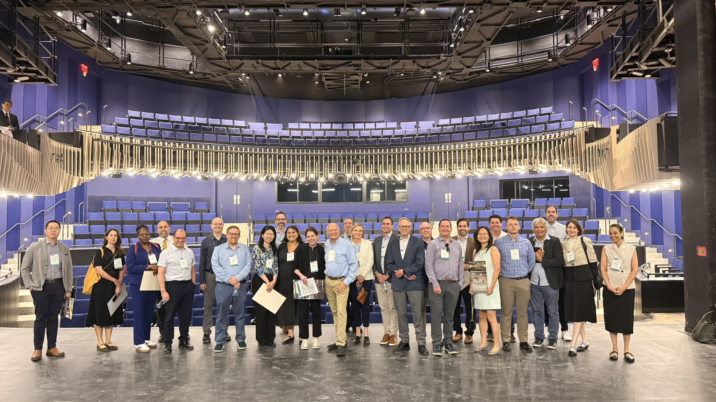 Group of people lined up on stage of recently constructed auditorium with blue seats