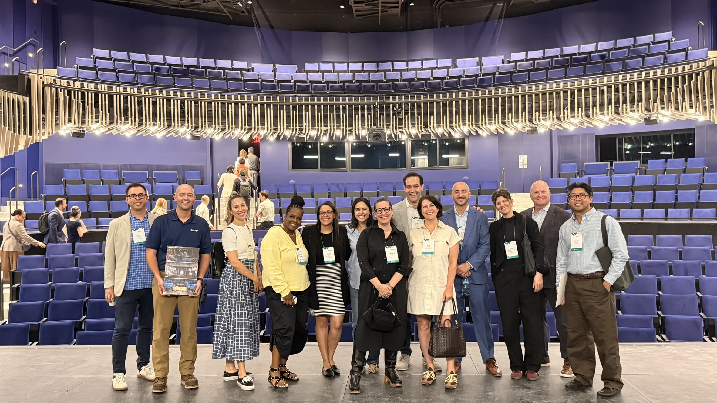 Group of people lined up on stage of recently constructed auditorium with blue seats